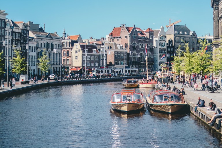 Boats on an Amsterdam canal with historic houses, illustrating guidance on the Dutch permit for residence processes.